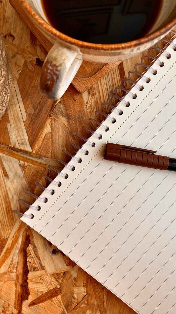 Spiral notebook and coffee cup on rustic wooden table. Ideal for writing inspiration.