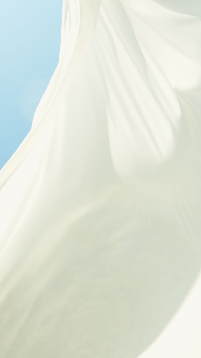 Elegant white fabric billowing against a clear blue sky, capturing lightness and freedom.