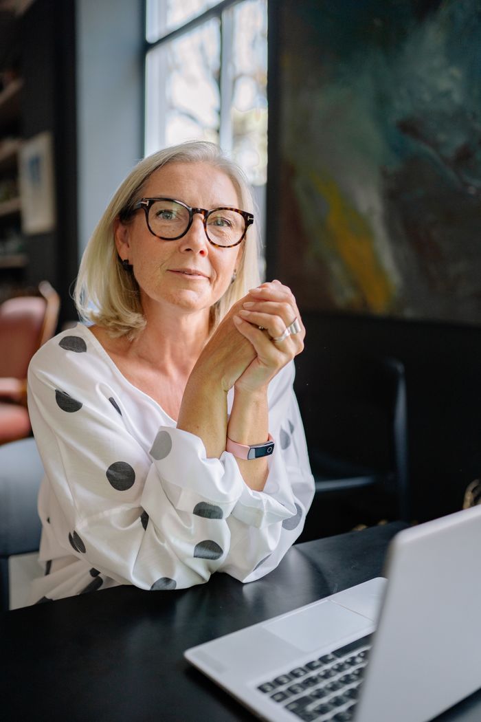 Senior woman with eyeglasses and polka dot blouse at a desk with a laptop. Bright and contemplative mood.